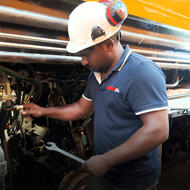 A man in a white hard hat inspects machinery while holding a wrench.